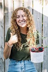 young woman holding a potted plant in front of a fence